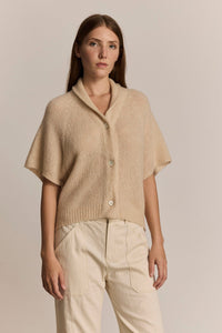 Woman wearing a beige short sleeve knit cardigan and pants against a plain background