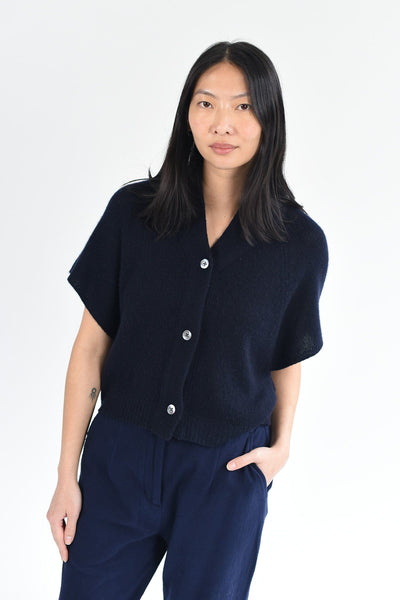 A woman wears the M.Patmos Ilam short sleeve, cashmere cardigan in navy blue with three buttons down the front. Designed in Brooklyn, New York.