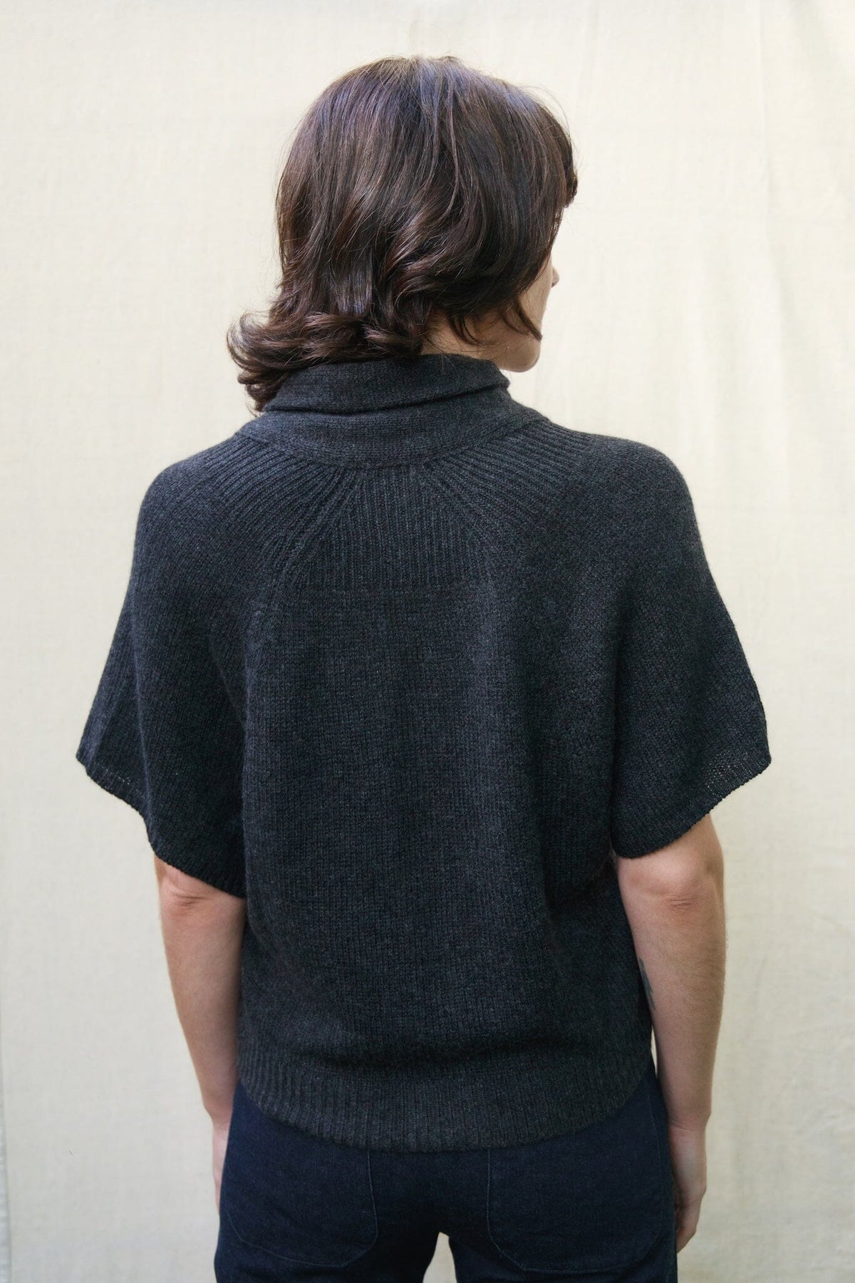 Woman wearing a charcoal short sleeve soft cashmere cardigan against a beige background