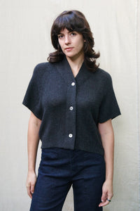 Woman wearing a charcoal short sleeve soft cashmere cardigan against a beige background