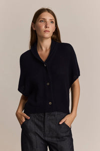 Woman wearing a navy short sleeve soft cashmere cardigan against a beige background