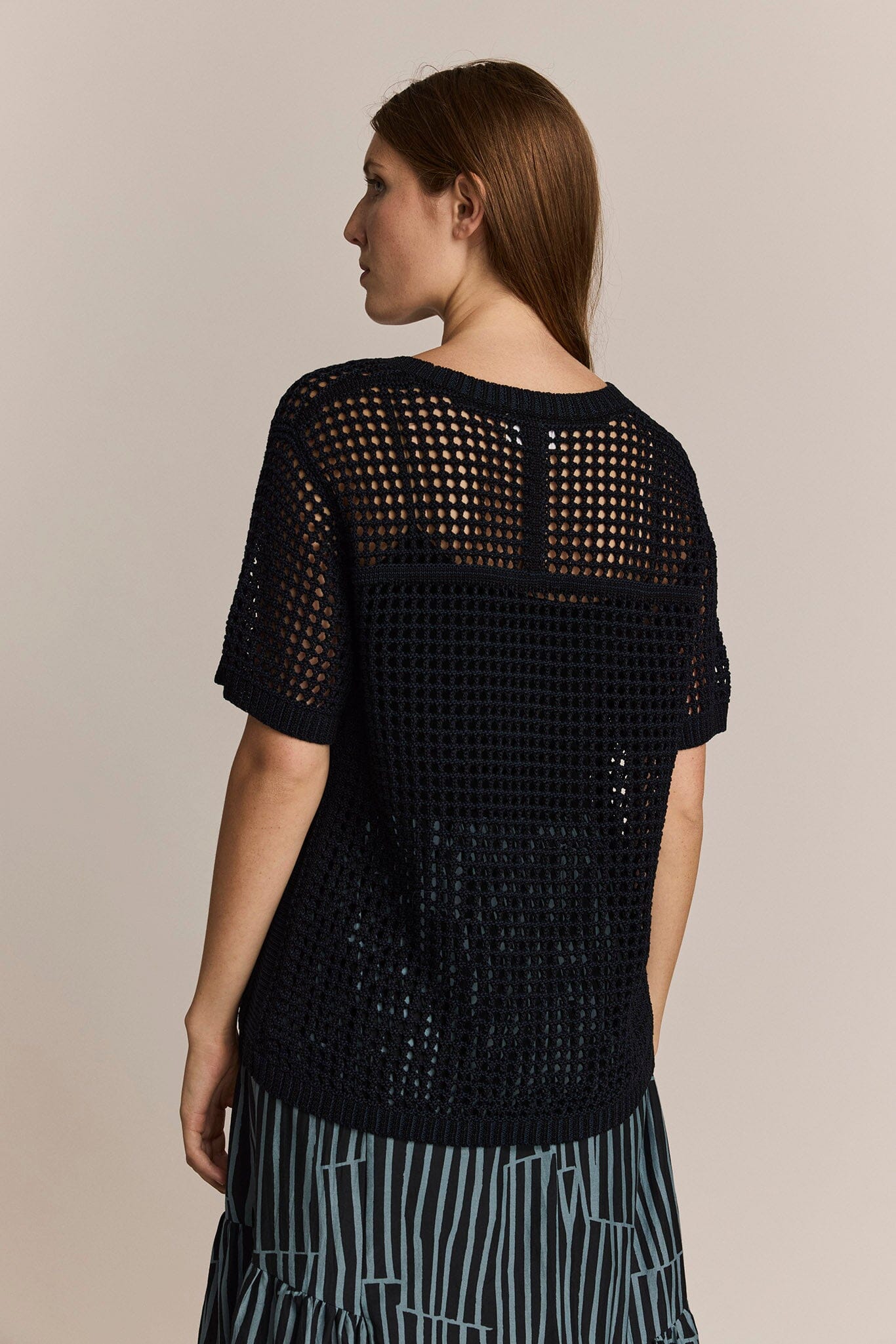 Woman wearing a black short sleeve knit top with a beige background