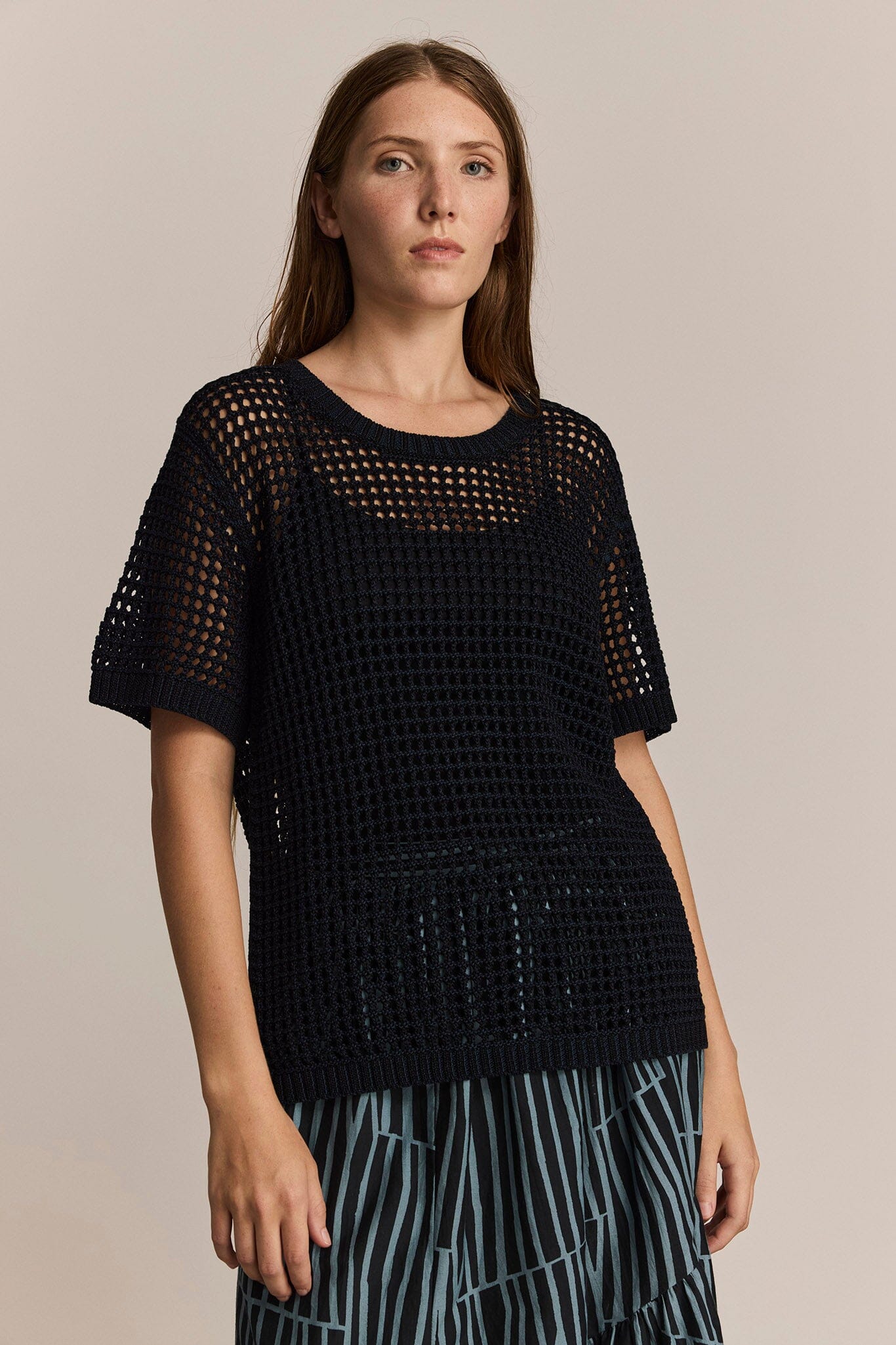 Woman wearing a black and navy short sleeve knit top with a beige background