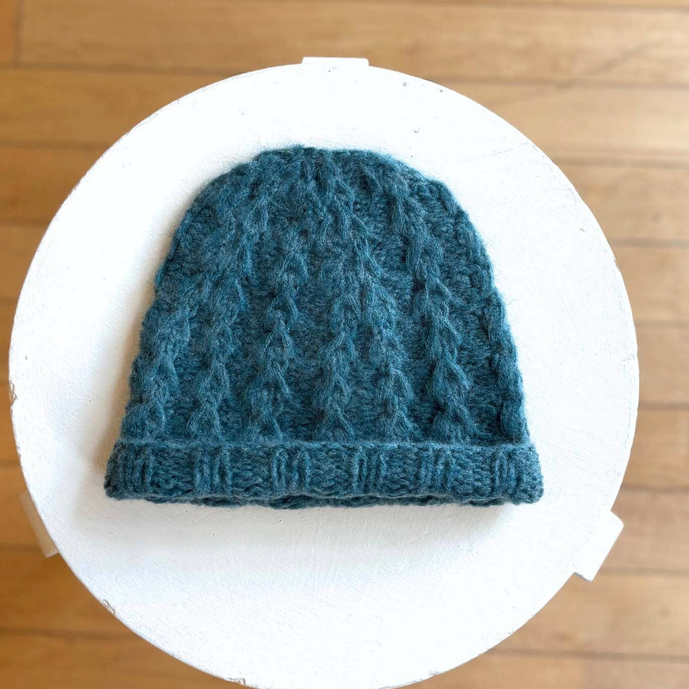 Green blue knitted hat on a white circular platform with a wooden floor background
