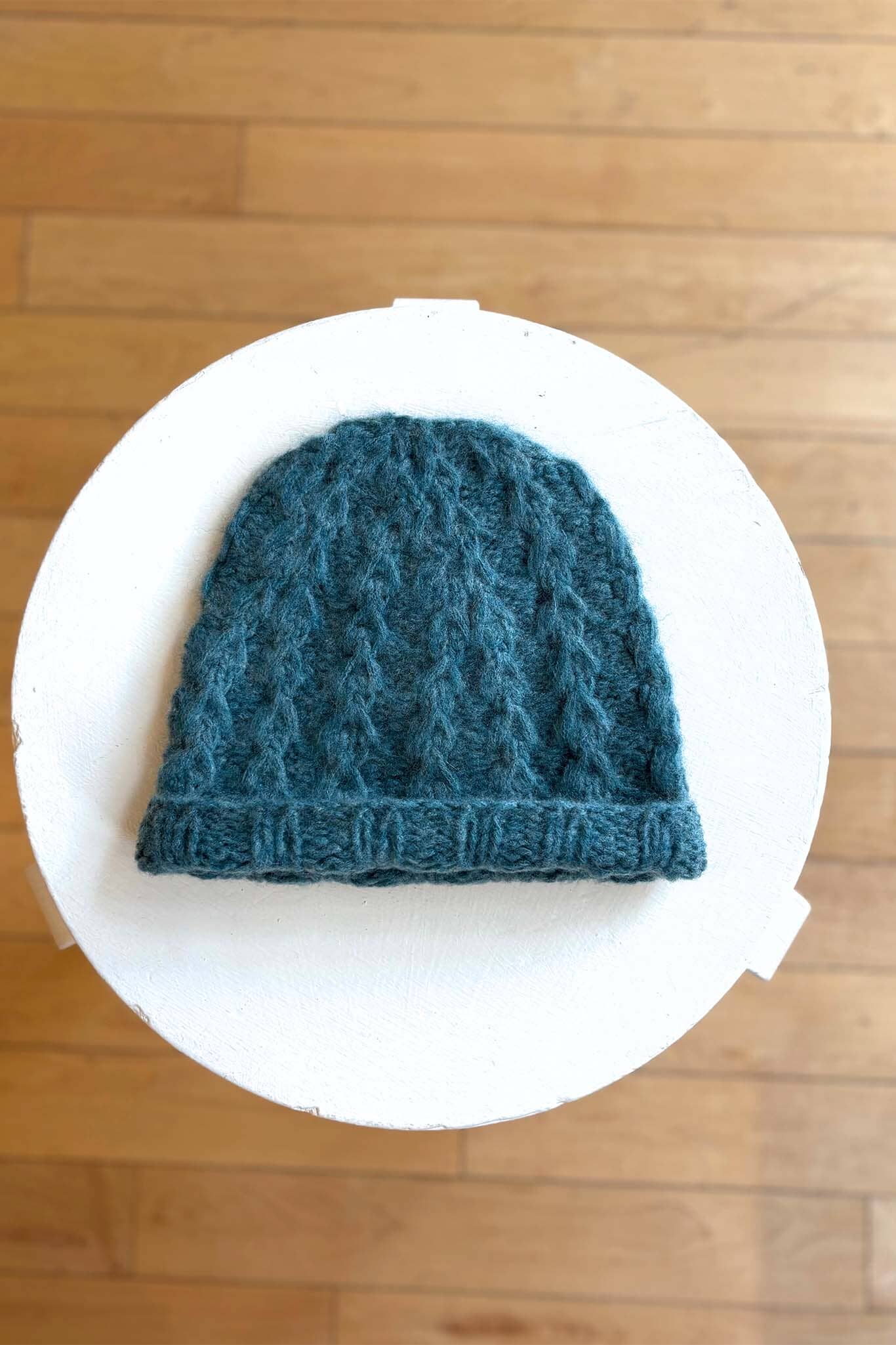 Green blue knitted hat on a white circular platform with a wooden floor background