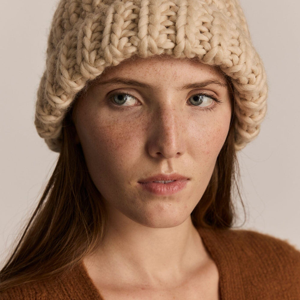 Woman wearing a beige knitted beanie against a neutral background