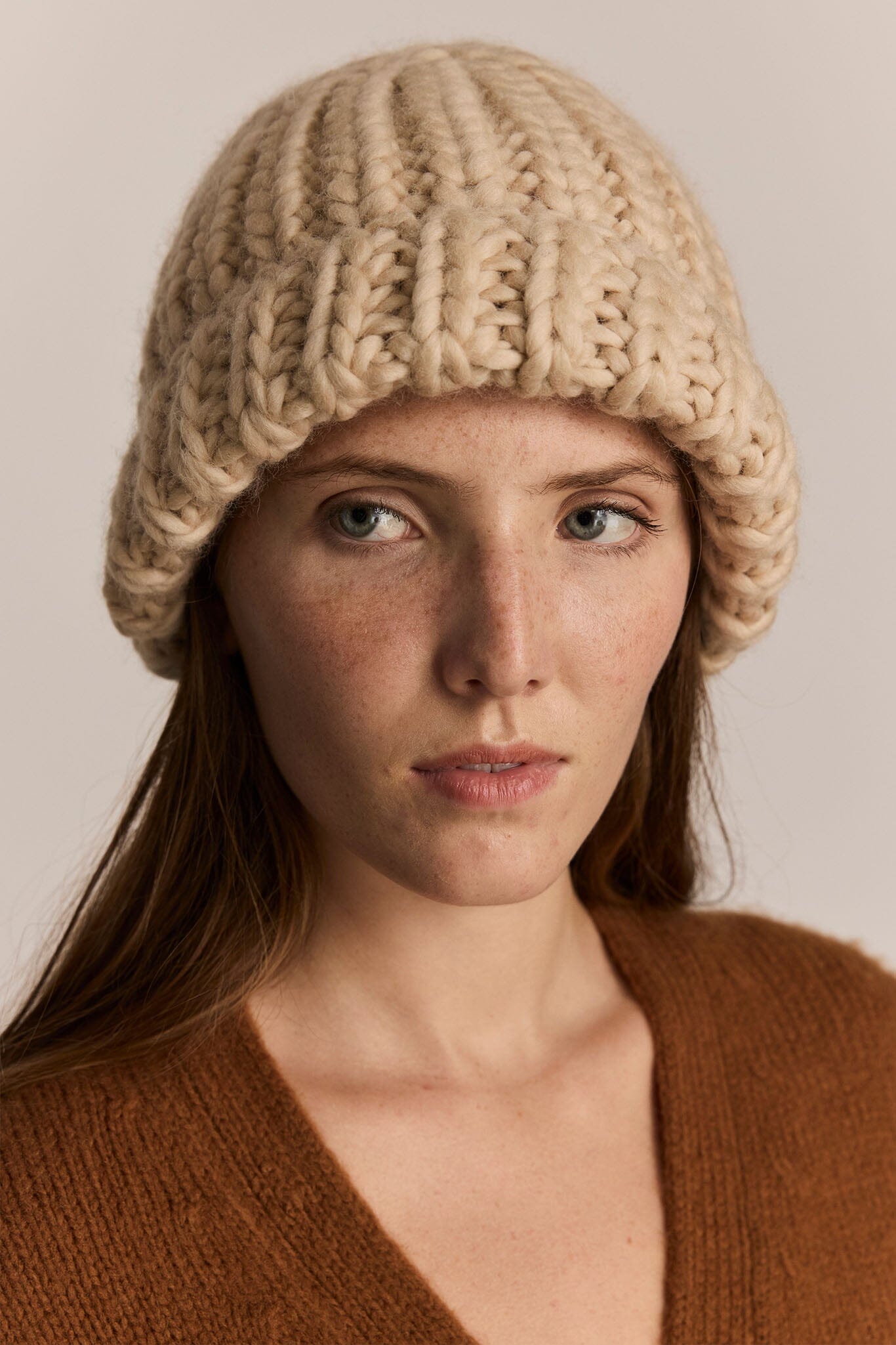 Woman wearing a beige knitted beanie against a neutral background