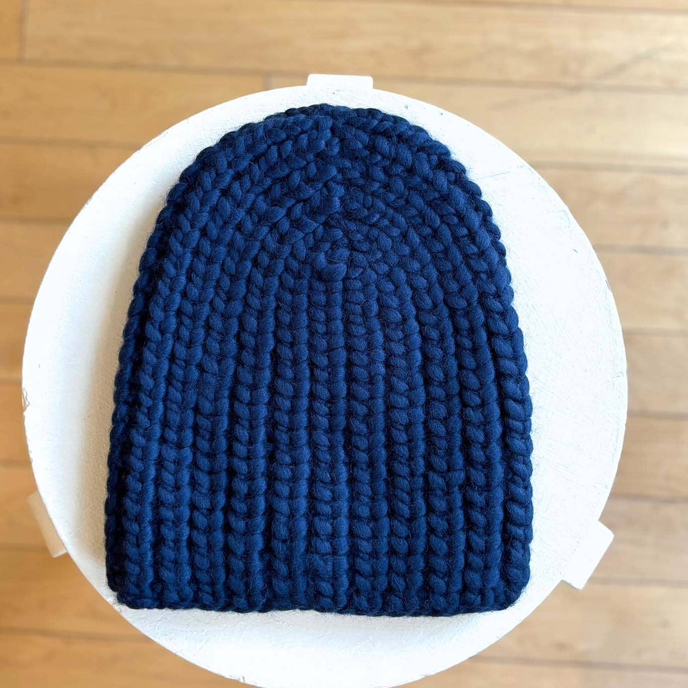 Navy knit beanie on a white plate with a wooden floor background