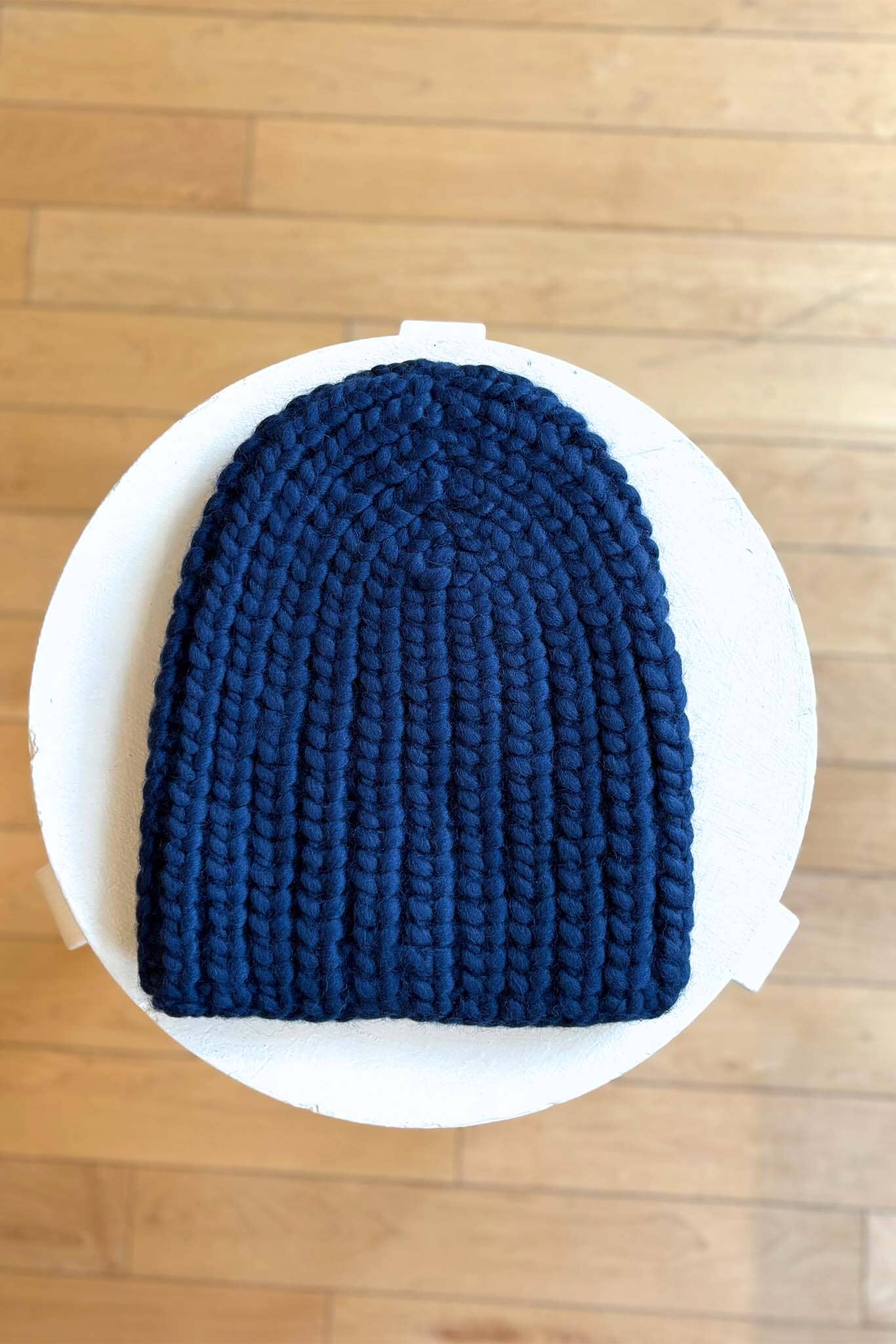 Navy knit beanie on a white plate with a wooden floor background