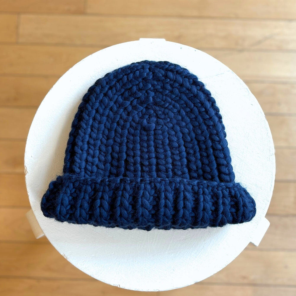 Blue knit hat on a white circular stand against a wooden floor background