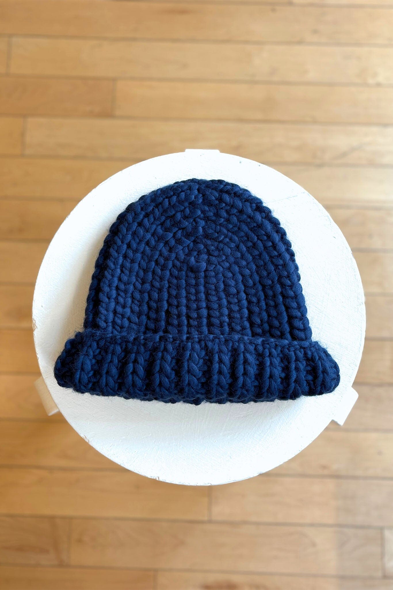 Blue knit hat on a white circular stand against a wooden floor background