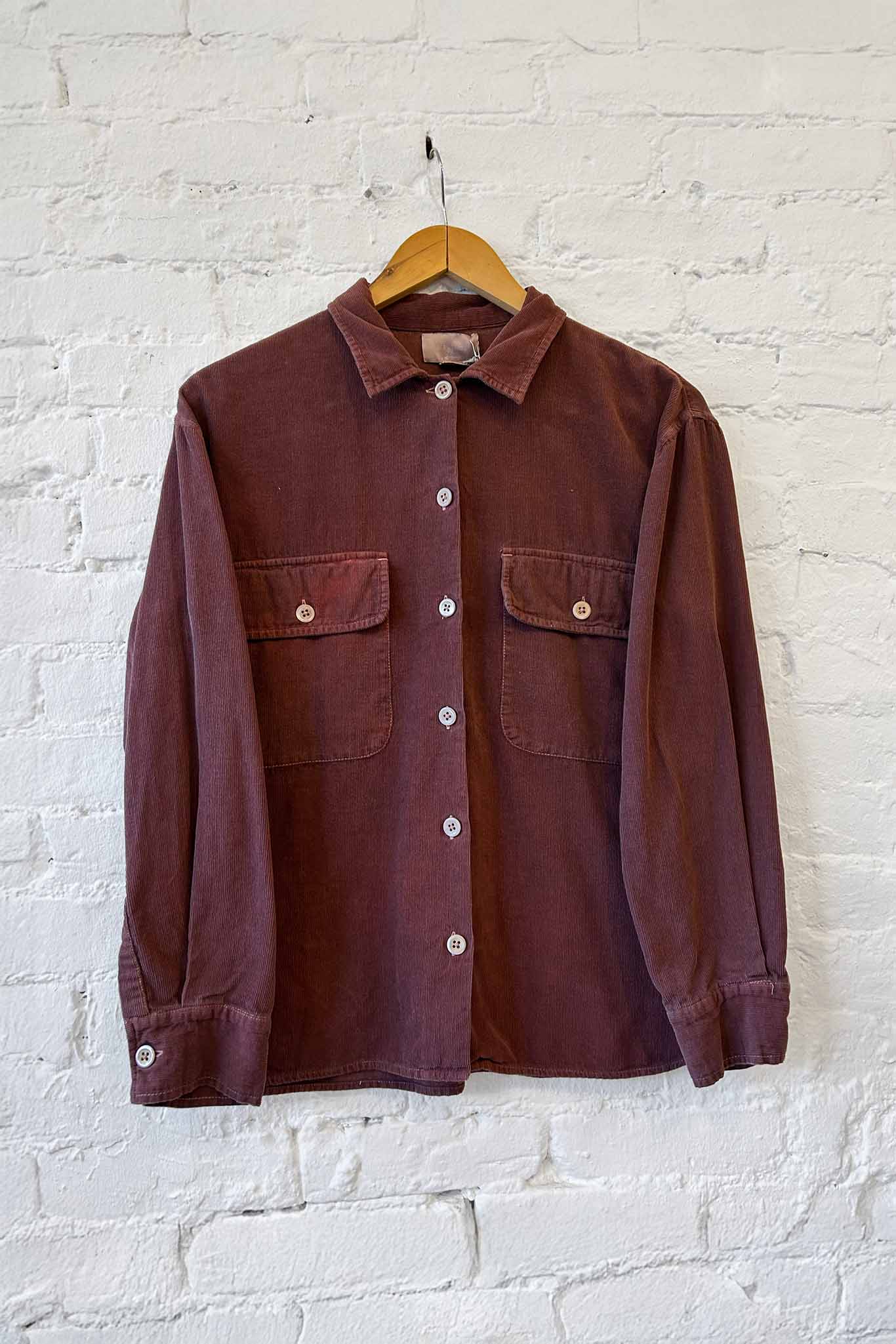 Berry long sleeve jacket on a hanger against a white brick wall