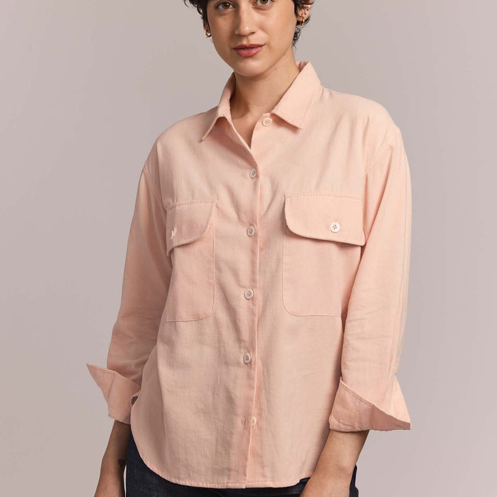 Person wearing a light pink button-up shirt against a plain background