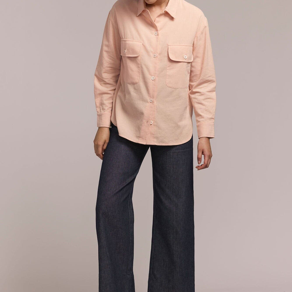 Person wearing a light pink shirt and dark blue pants on a plain background