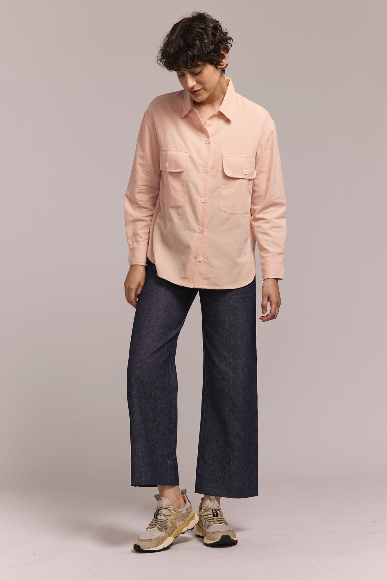 Person wearing a light pink shirt and dark blue pants on a plain background