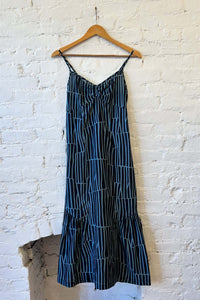 Black and blue striped dress on a wooden hanger against a white brick wall.