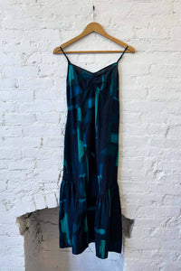 Blue patterned dress on a wooden hanger against a white brick wall.
