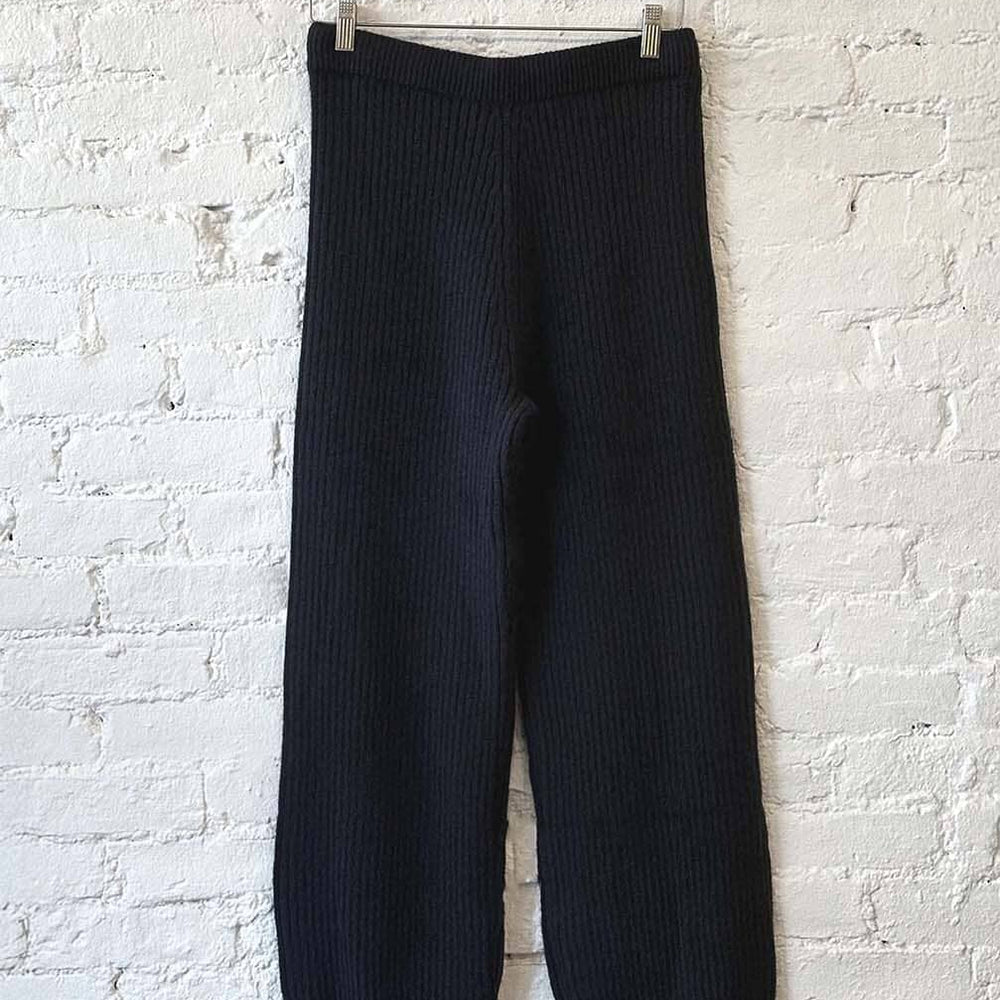 Black ribbed knit pants hanging against a white brick wall.