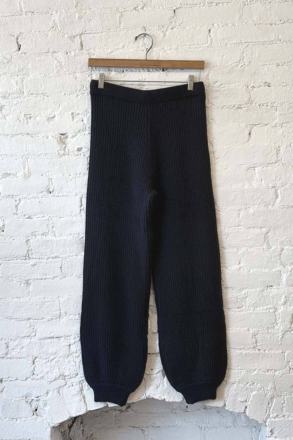 Black ribbed knit pants hanging against a white brick wall.