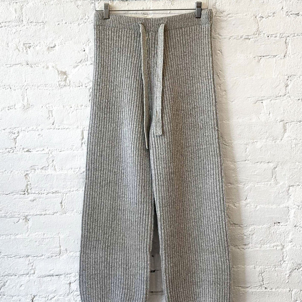 
                  
                    Gray knit pants hanging on a wooden hanger against a white brick wall.
                  
                