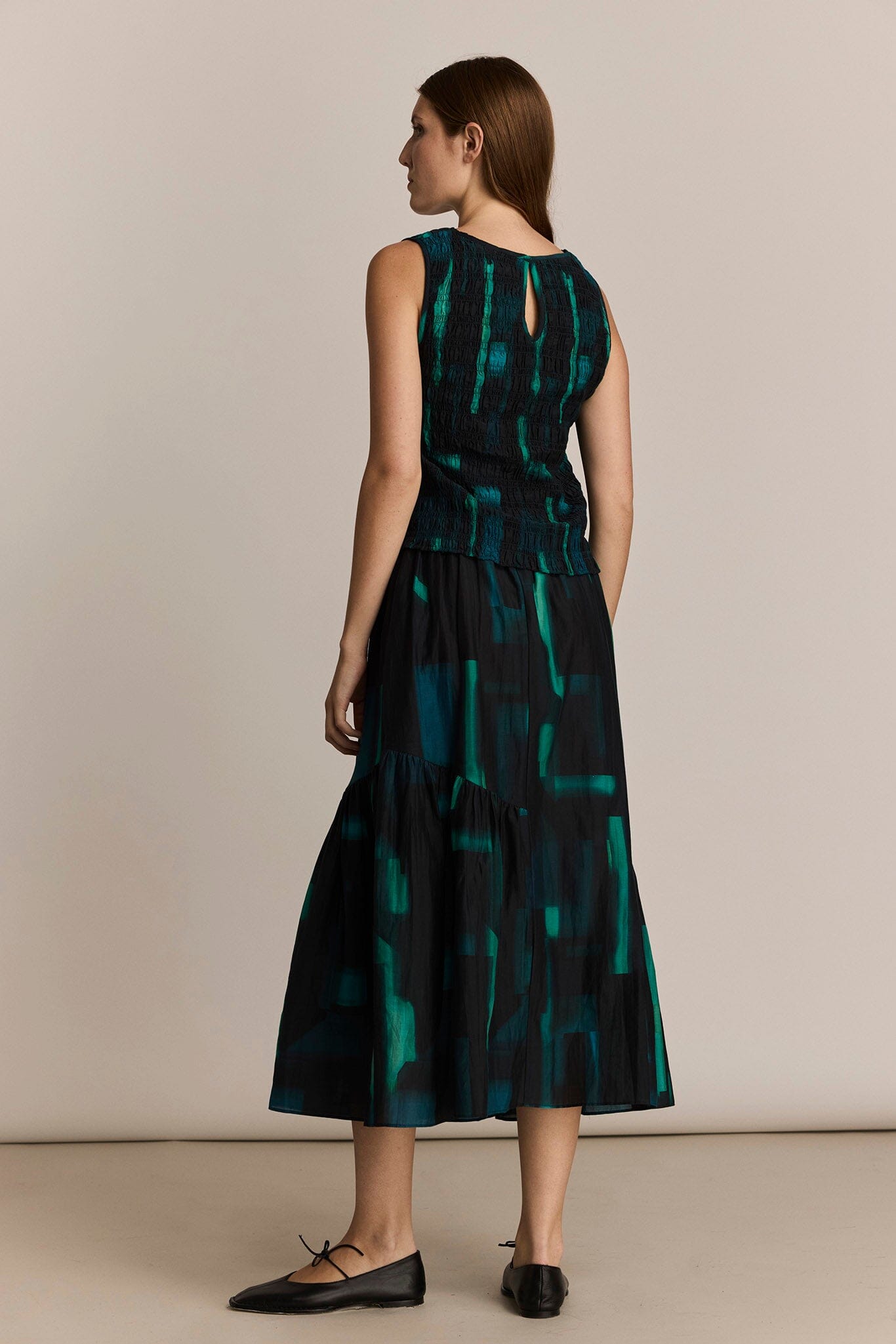 Woman wearing a black and green patterned dress against a beige background