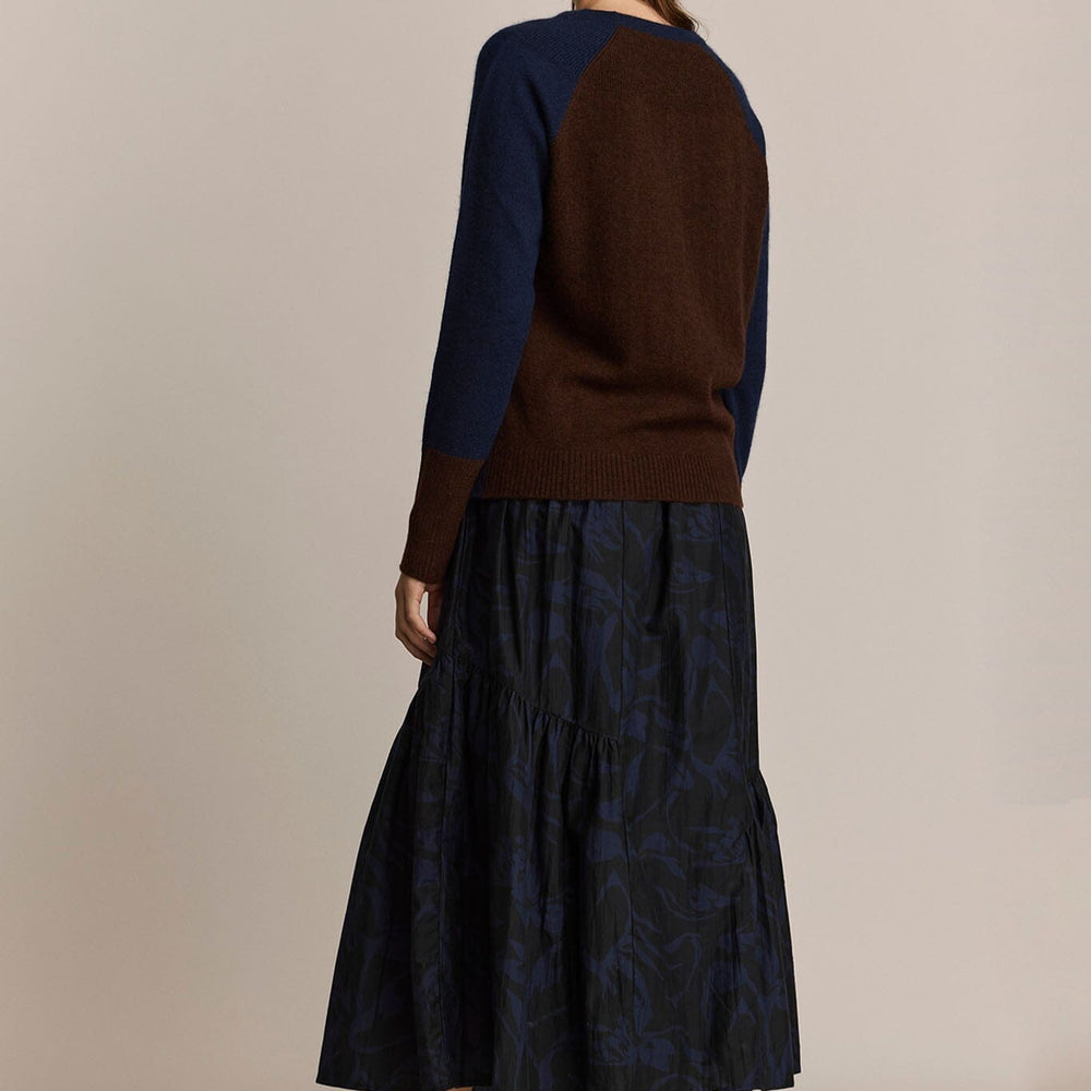 
                  
                    Woman wearing a brown sweater and dark blue patterned skirt on a beige background
                  
                