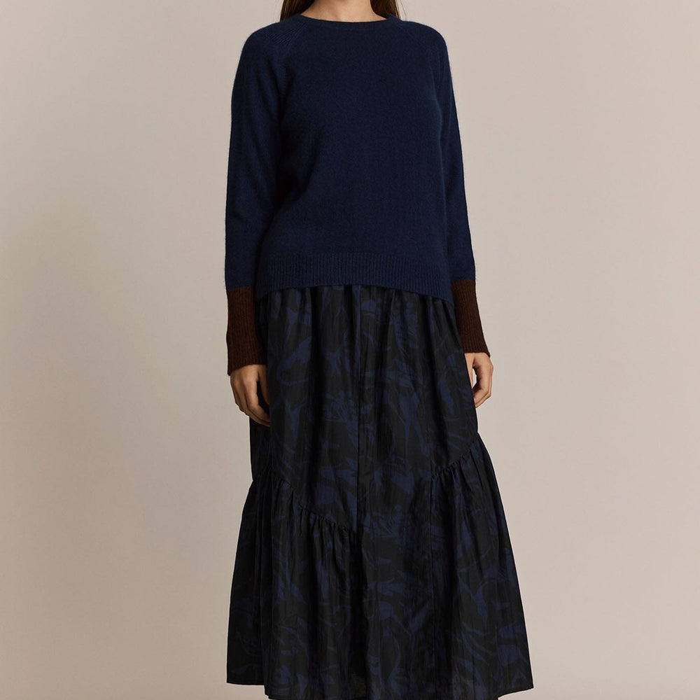 
                  
                    Woman wearing a navy blue sweater and patterned navy skirt against a beige background
                  
                