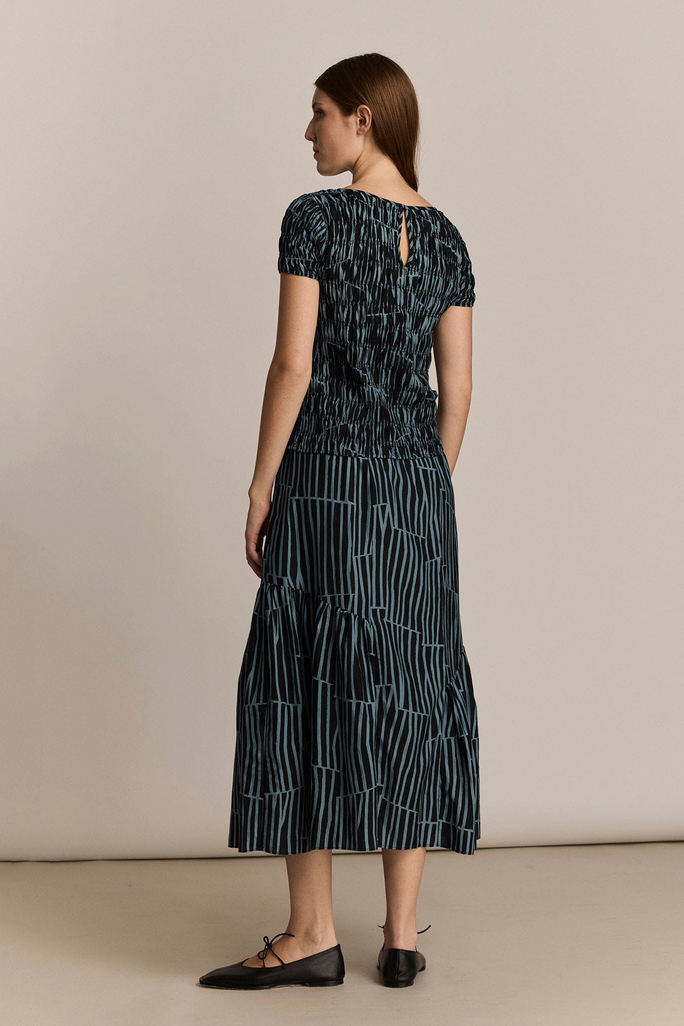 Woman facing the back wearing a black and dark blue skirt with an organic striped pattern against a beige background