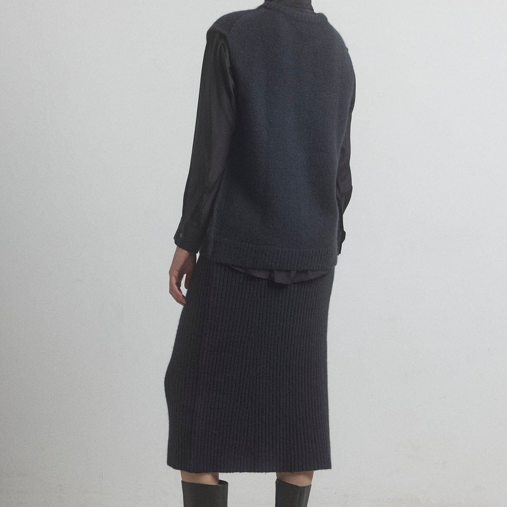 Woman facing the back wearing a black merino vest and skirt on a white background