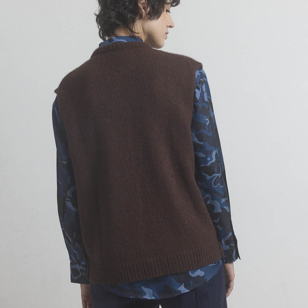 
                  
                    Woman wearing a brown merino vest over a patterned shirt on a plain background
                  
                