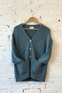 Blue green cardigan on a wooden hanger against a white brick wall