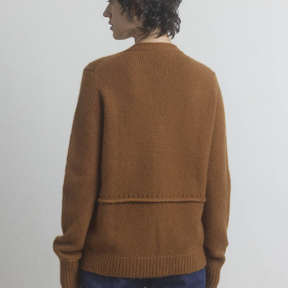 Woman wearing a brown cashmere and wool sweater and blue jeans against a plain background.