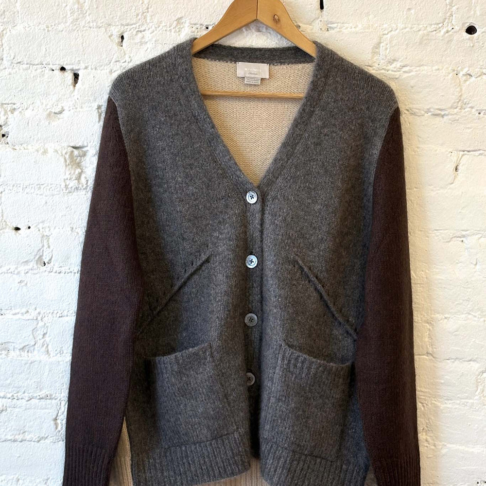 
                  
                    Gray and brown two-toned cardigan on a wooden hanger against a white brick wall
                  
                