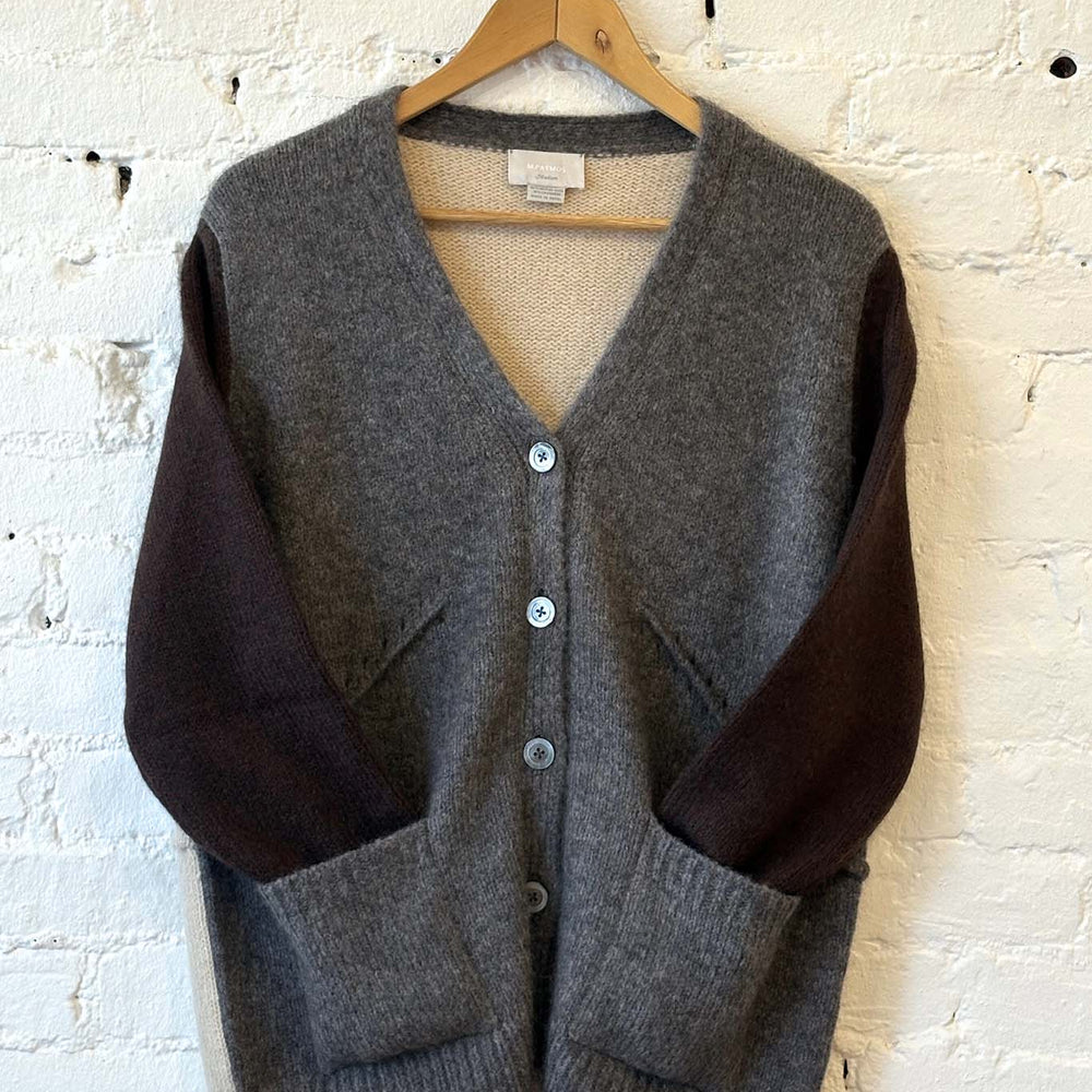 
                  
                    Two-tone cardigan on a hanger against a white brick wall
                  
                