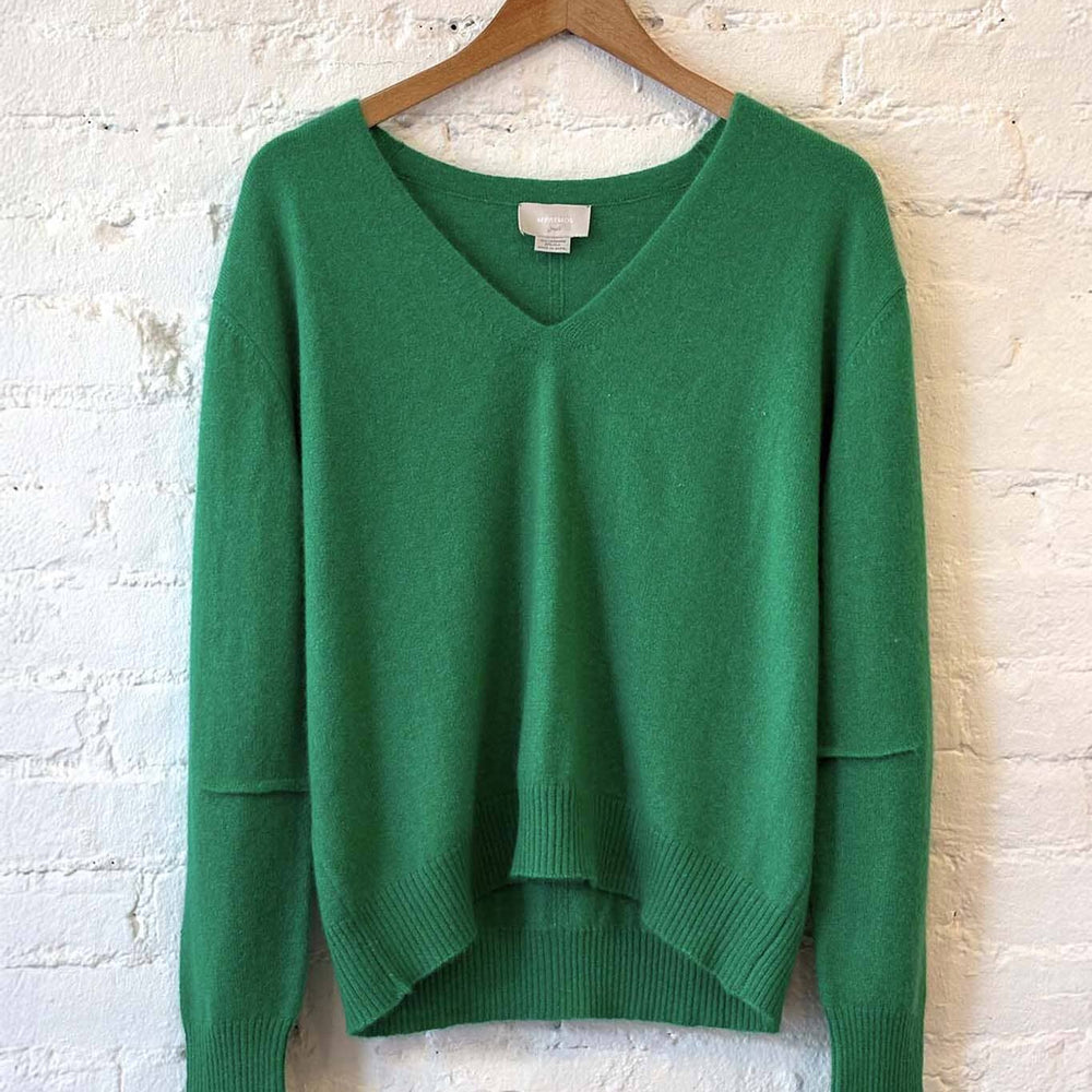 
                  
                    Green v-neck sweater on a wooden hanger against a white brick wall
                  
                