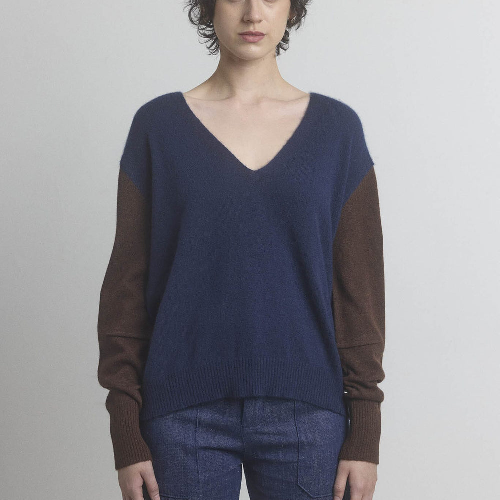 Woman wearing a two-tone navy sweater with brown sleeves on a plain background