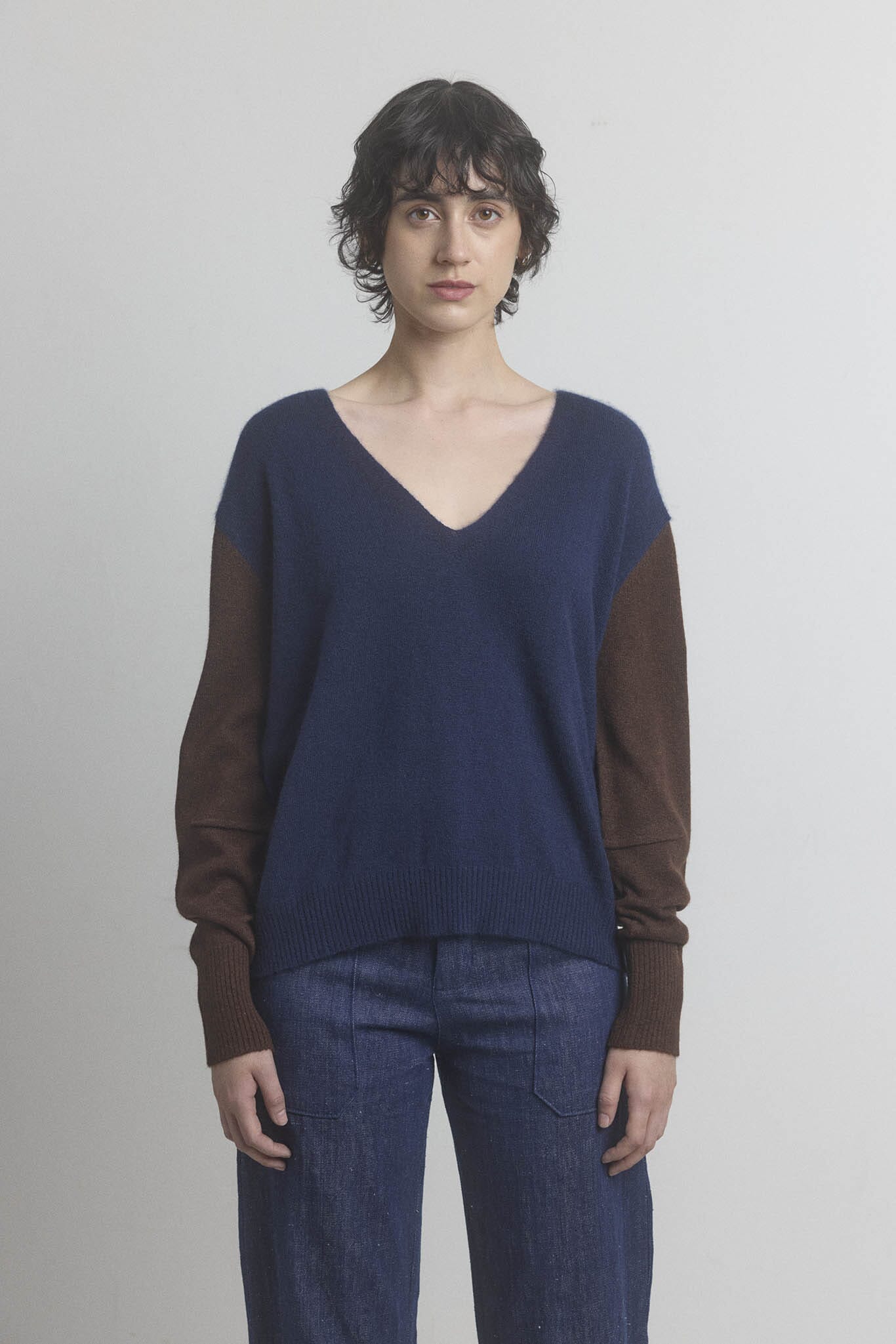 Woman wearing a two-tone navy sweater with brown sleeves on a plain background