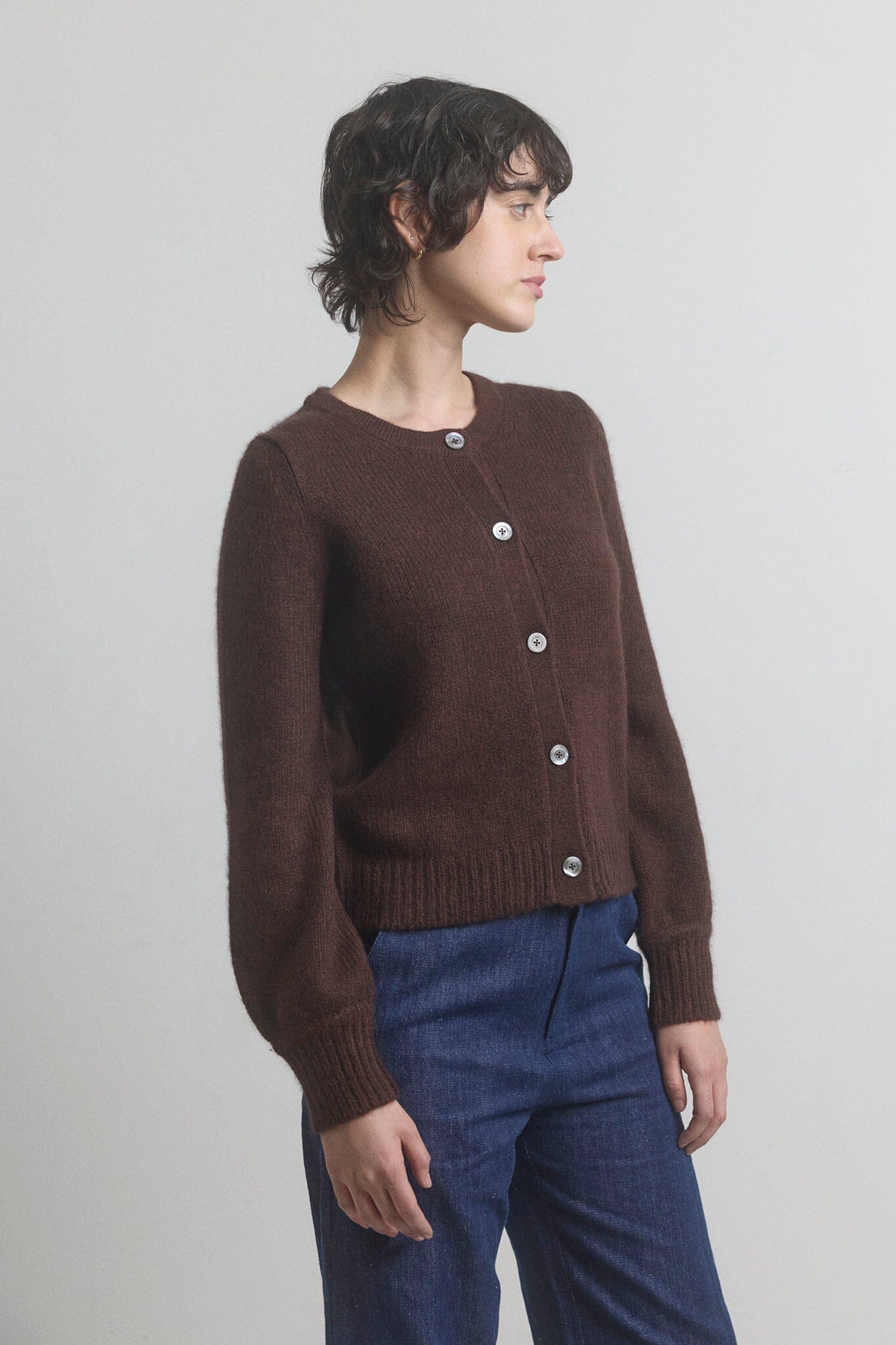 Woman wearing a brown wool and silk blend M.PATMOS cardigan with silver buttons on a plain background.