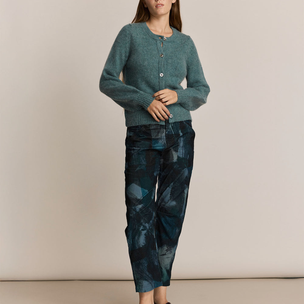 Woman wearing a green knitted cardigan and patterned pants against a beige background