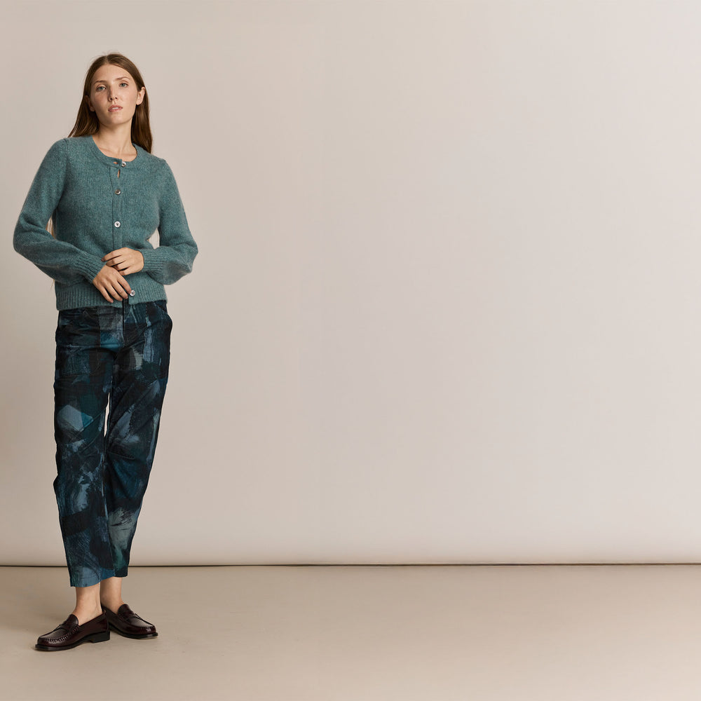 Woman wearing a green knitted sweater and pants against a plain background