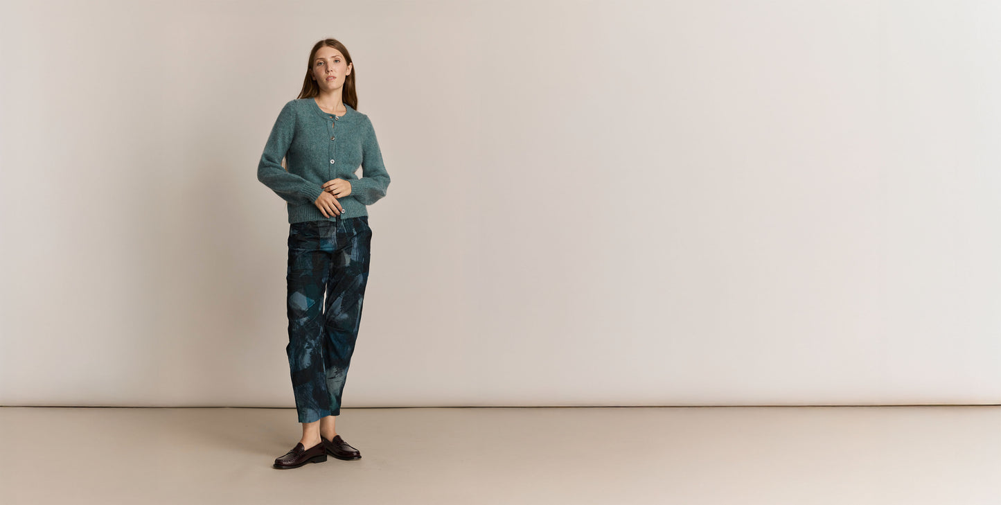 Woman wearing a green knitted sweater and pants against a plain background