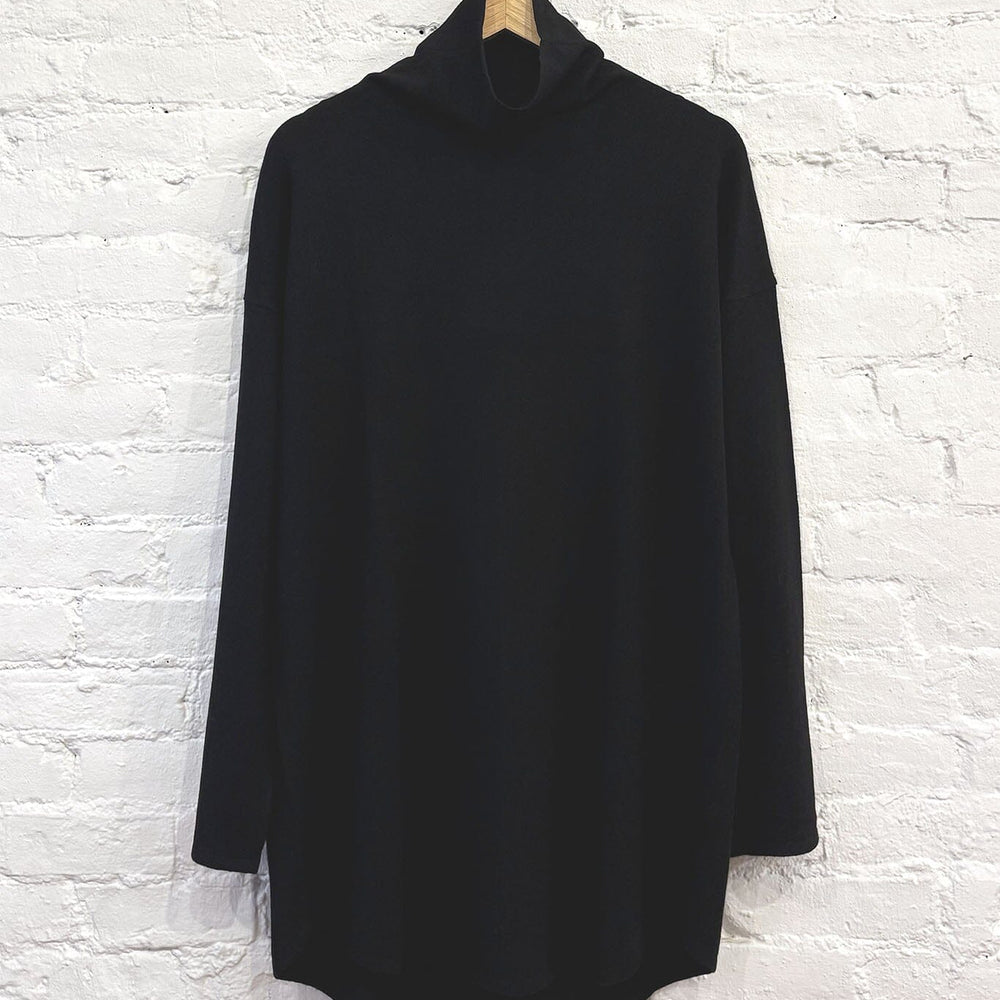 Black cashmere turtleneck sweater hanging against a white brick wall