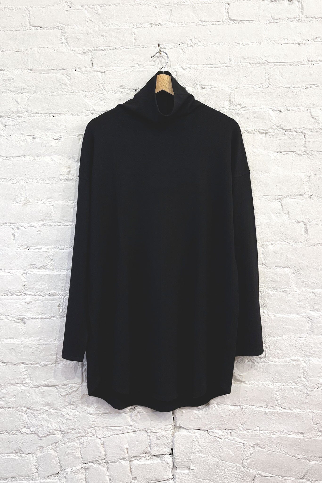 Black cashmere turtleneck sweater hanging against a white brick wall