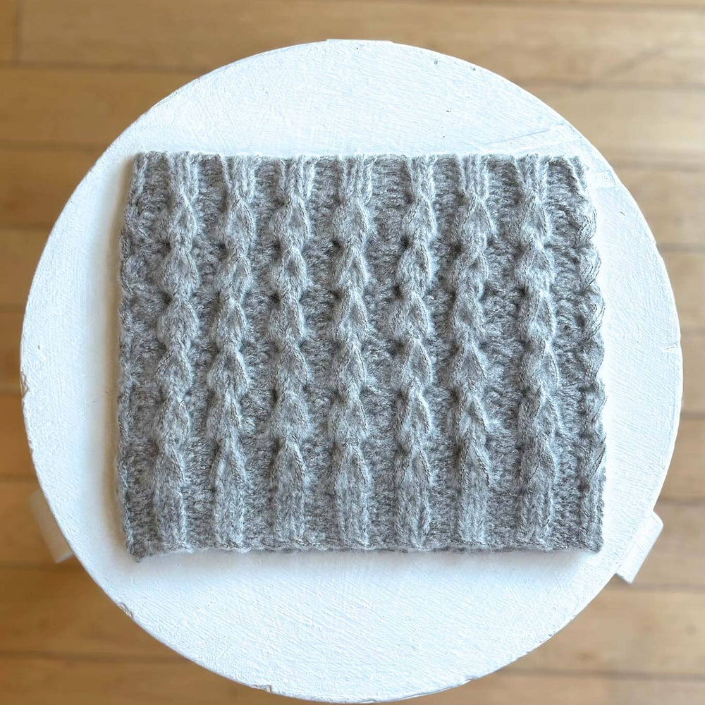 Gray textured square funnelneck on a white circular platform with a wooden floor background