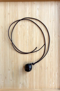 Black circular stone cord necklace on a light wood background