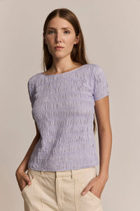 Woman wearing a light purple textured top against a beige background