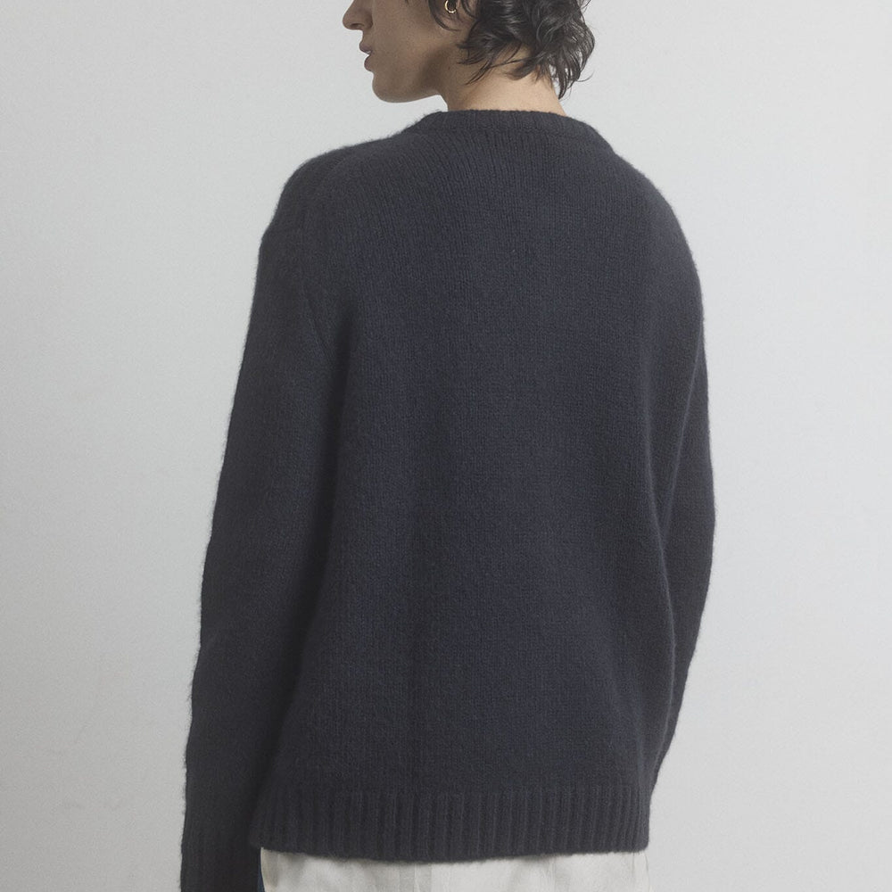 Woman facing the back wearing a merino wool sweater over a white shirt with a plain background