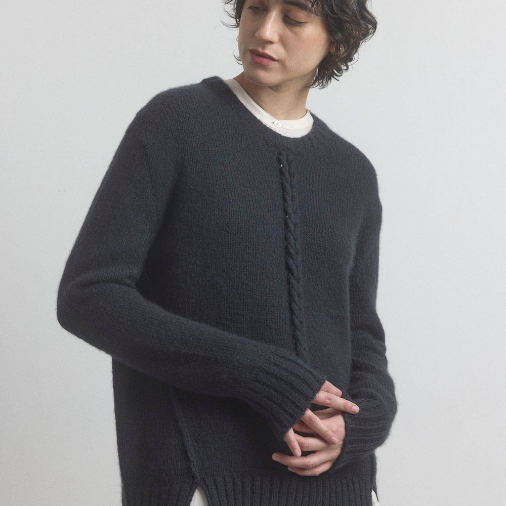Woman wearing a black sweater over a white shirt on a plain background