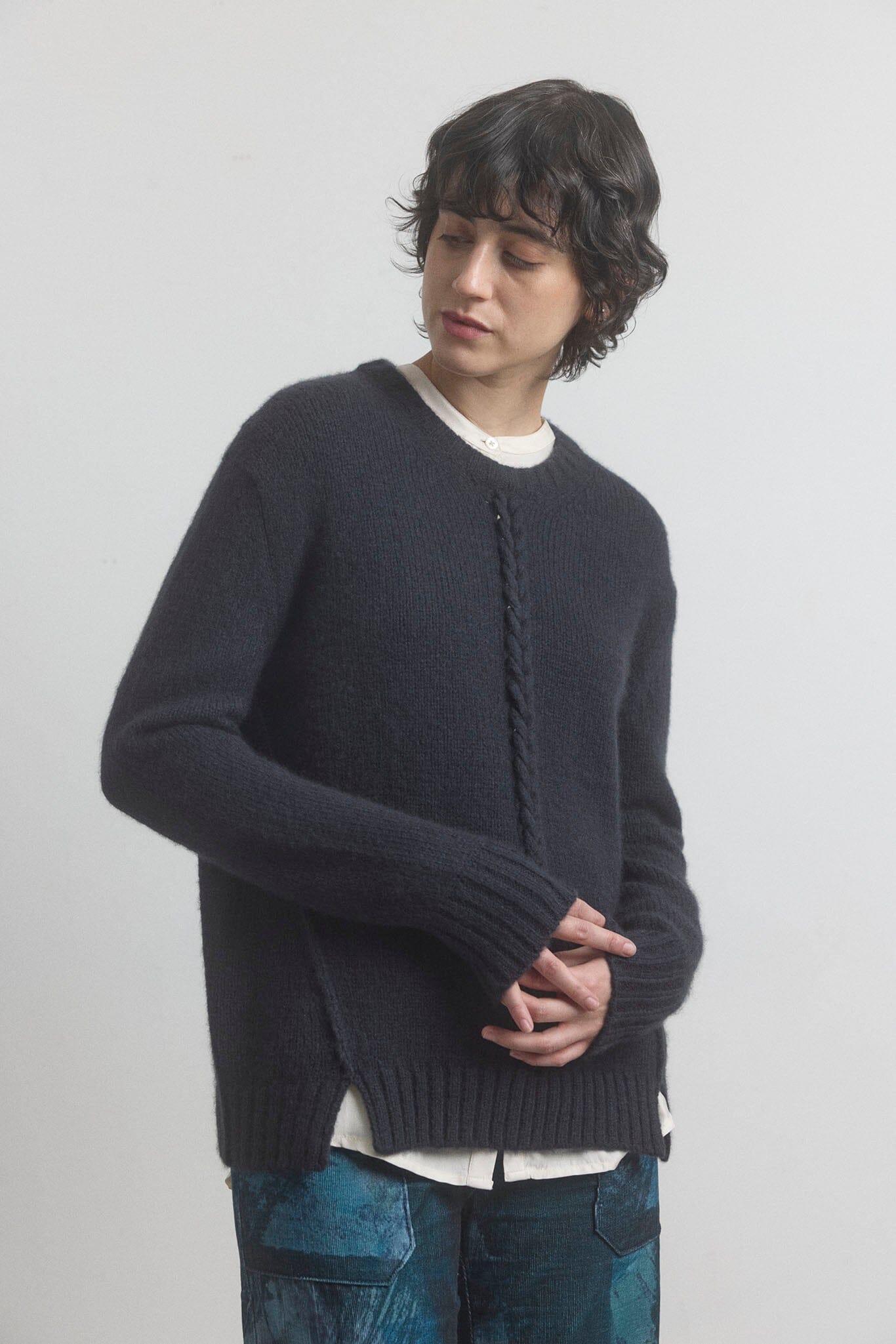 Woman wearing a black sweater over a white shirt on a plain background