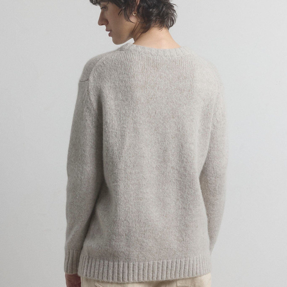 Woman wearing a gray sweater and beige pants against a plain background